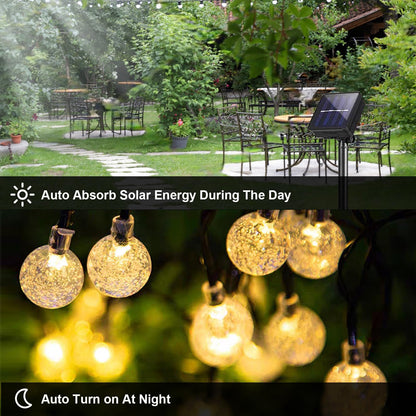 Solar-Lichterkette mit warmweiß leuchtenden Glaskugeln und Solarpanel im Garten