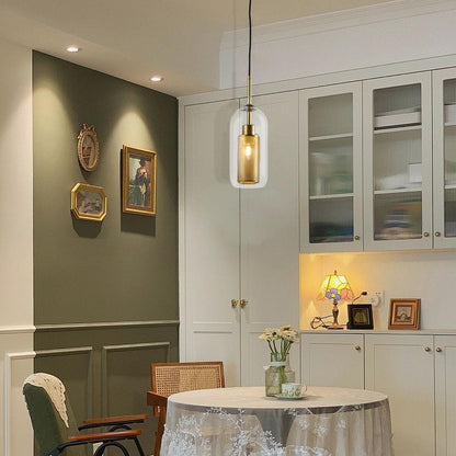 Pendelleuchte mit goldenem Metallgehäuse und klarem Glasschirm im Raum