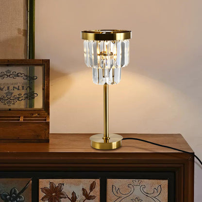 Kristall-Tischlampe mit goldfarbenem Fuß und zylindrischem Kristallschirm auf Holzoberfläche