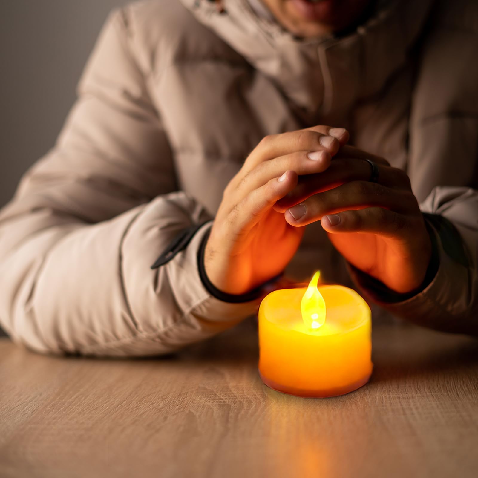 Hand hält eine gelbe LED-Teelicht-Kerze, warm flackernde Flamme auf dem Tisch
