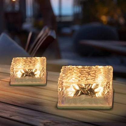 Zwei goldfarbene Solar-Glaswürfelleuchten auf Holzplatte, warmweiß beleuchtet