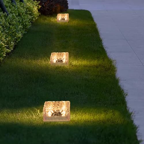 Drei goldene Solar-Glaswürfelleuchten im Rasen, warmweiß beleuchtet